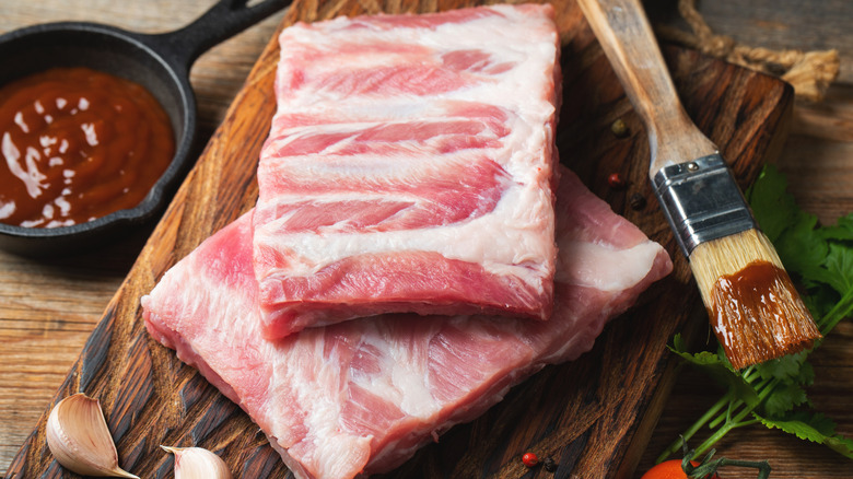 Raw ribs on a cutting board with a basting brush with barbecue sauce