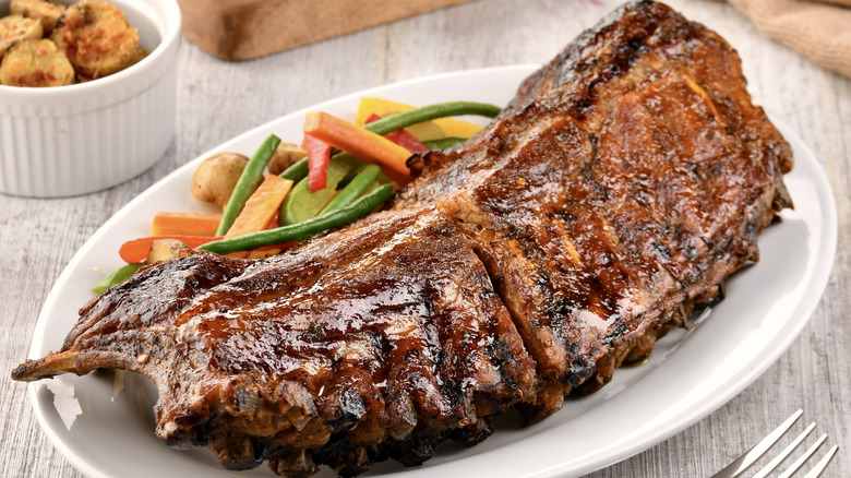 Rack of cooked ribs with vegetables on a white plate