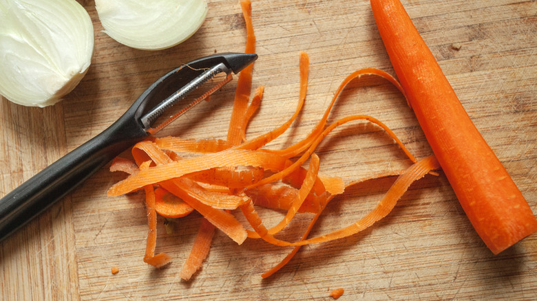 A peeled carrot with skins and a peeler on the side