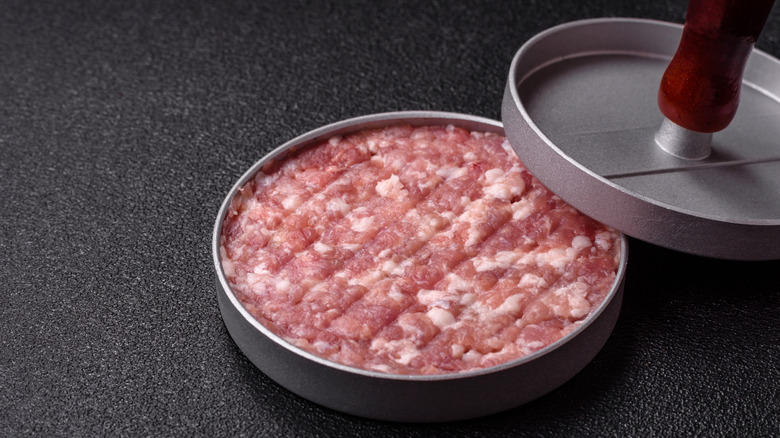 A burger press filled with ground meat.