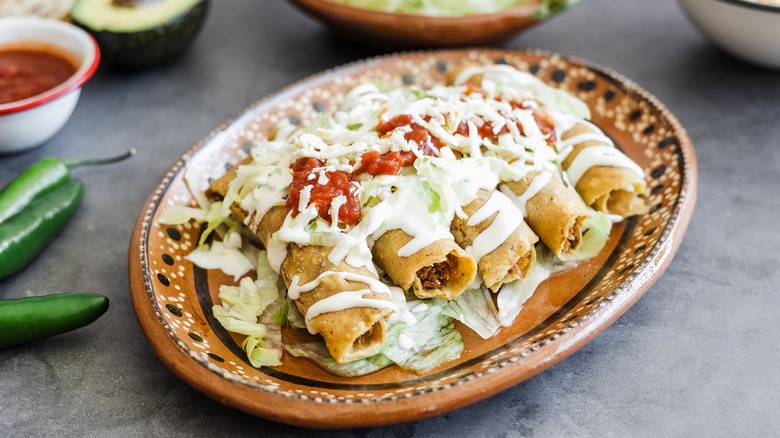 A plate of tacos durados with a generous dizzle of sauces on top