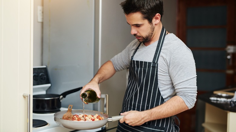 Person adding wine to a pan on a stove