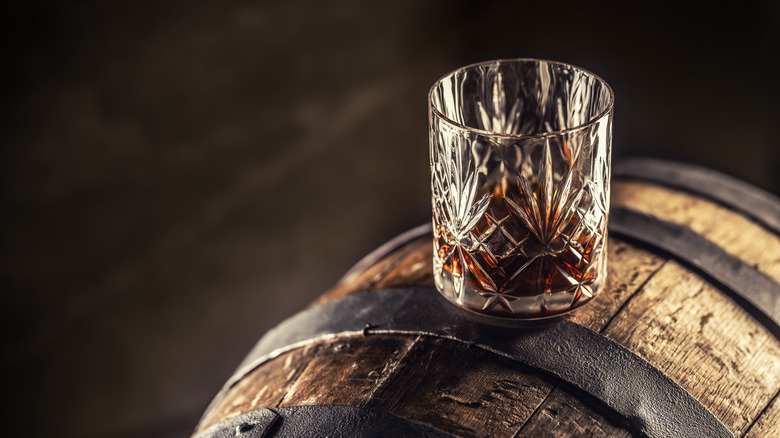 a glass of whiskey sitting on a barrel