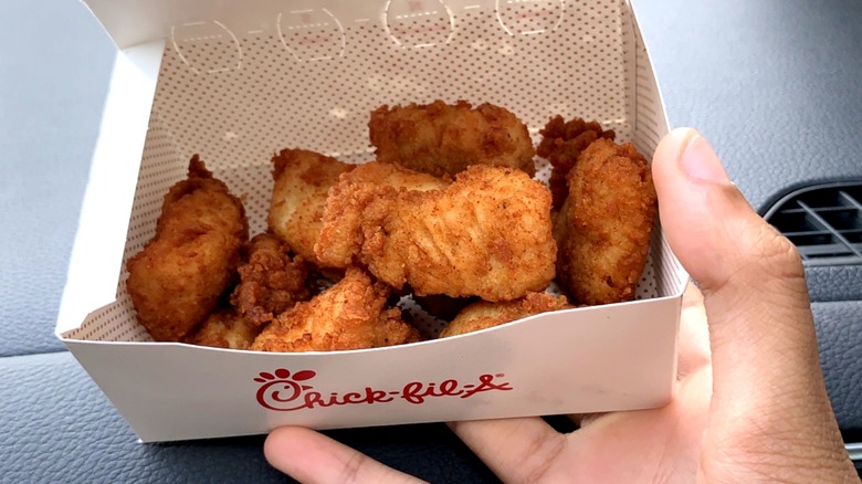 A person holds a carryout box of Chick-fil-A chicken nuggets inside their car