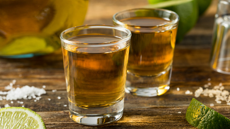 Two shots of añejo tequila with lime slices and salt