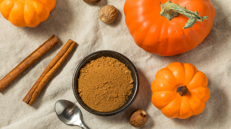 A bowl of spice surrounded by pumpkins, nutmeg, and cinanmon sticks