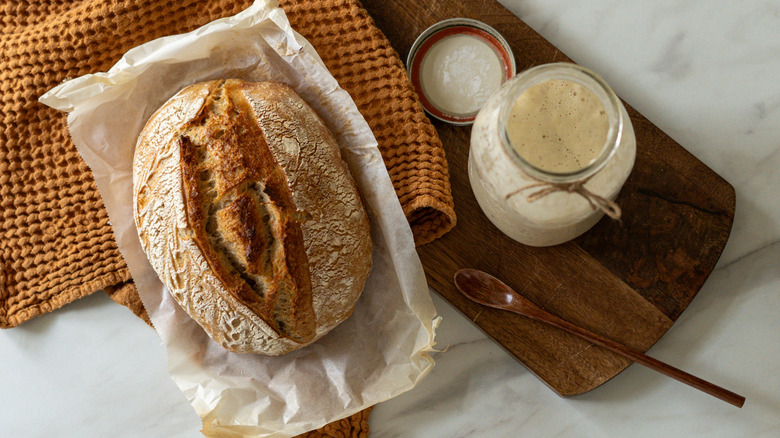 loaf of sourdough bread beside starter in jar