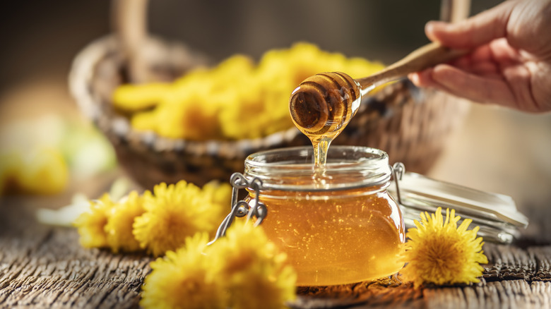Jar of honey surrounded by dandelions