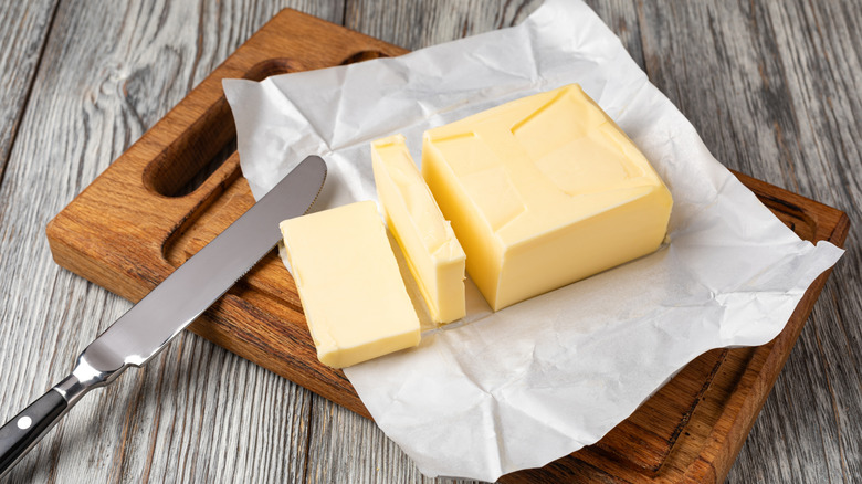 A block of butter with slices made on a cutting board.