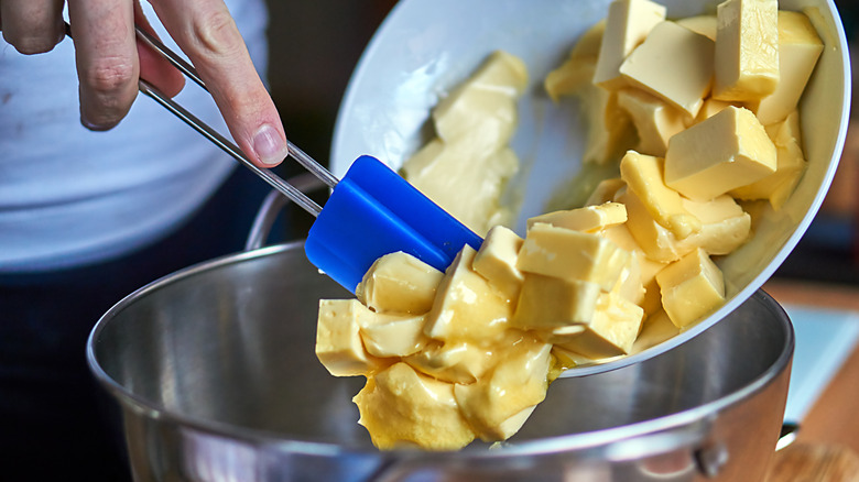 A person moves butter cubes into a bowl with a spatula.