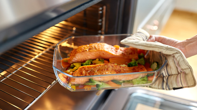 A cook placing a baking dish containing salmon and vegetables in the oven
