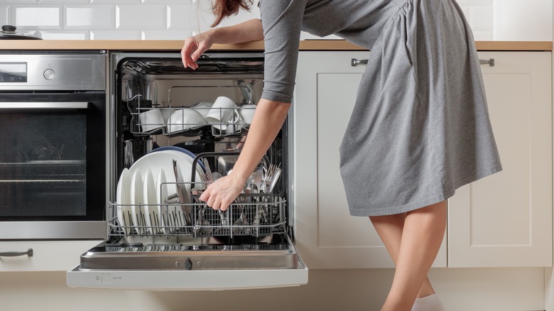 Woman in gray dress loading a dishwasher