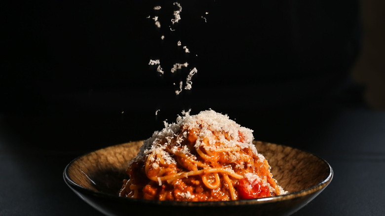 Close-up of grated parmesan cheese landing on a bowl of fresh, saucy spaghetti
