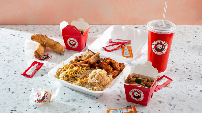 Panda Express takeout on a counter, including sauces, a drink, fried rice, chow mein, egg rolls, and other items