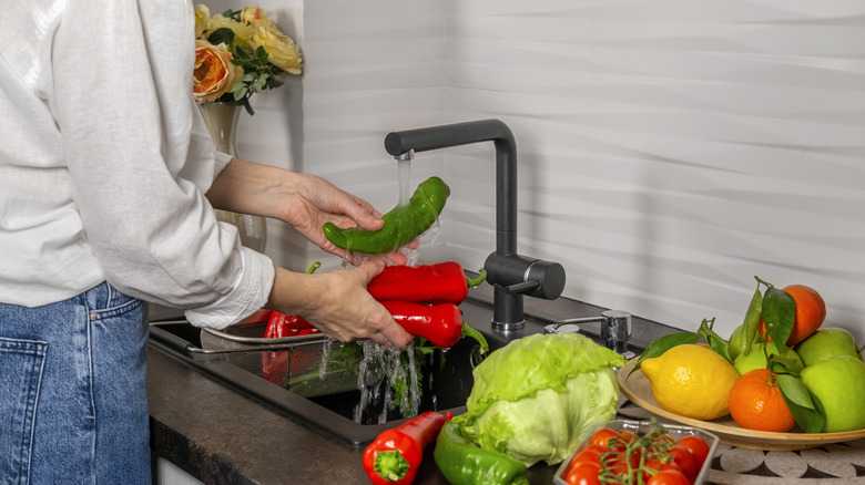 A woman washes vegetables under the tap in a sink