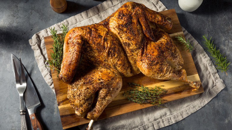 A spatchcocked chicken is served on a wooden board surrounded by herbs