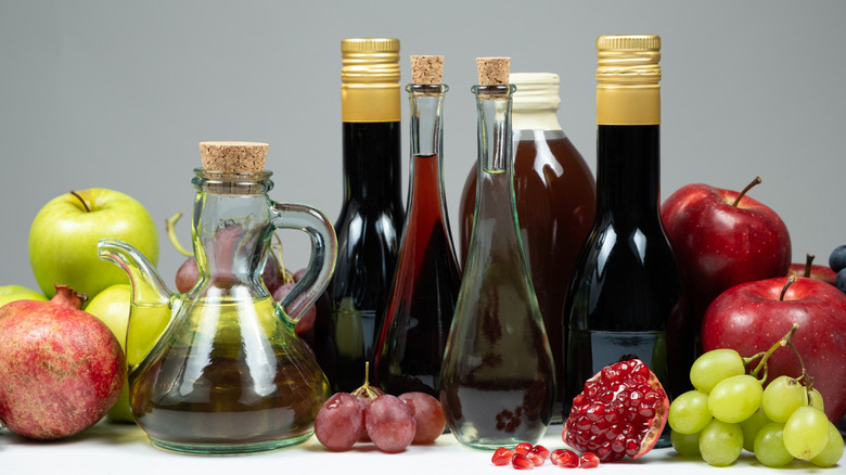 Several bottled vinegar varieties are arranged with various fruits.