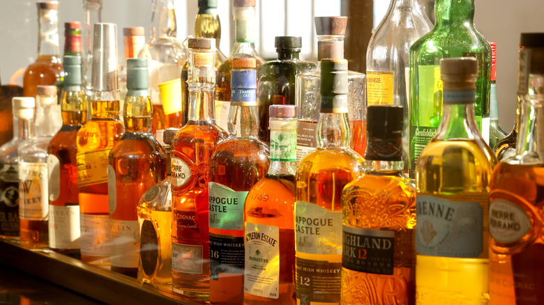 Dozens of bottles of spirits, including whiskey, on shelf.