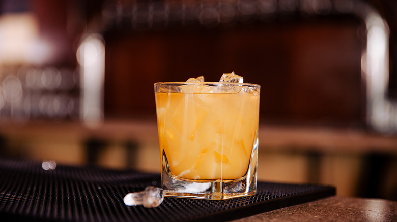 orange cocktail with ice in a rocks glass sitting on a bar