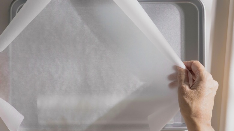 A baker's hand laying parchment paper over a clean baking sheet.