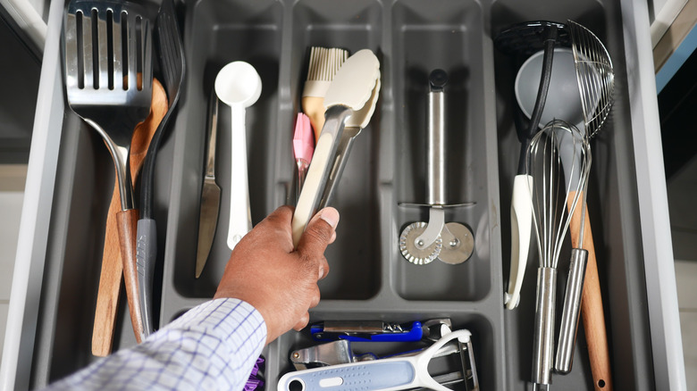 A hand reaching into a kitchen drawer filled with various tools