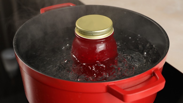 Jar of red jam half submerged in boiling water on stove