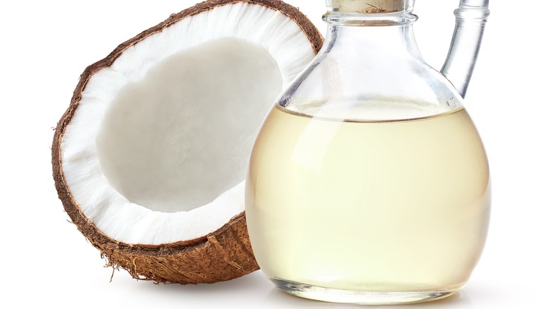 Half a coconut next to a glass bottle of liquid coconut oil