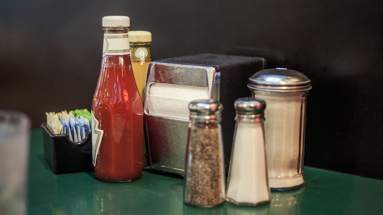 Dispensers and bottles of napkins, ketchup, mustard, salt, sugar, and pepper on a green table