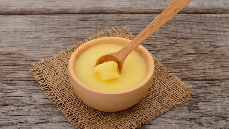 Bowl of ghee with a wooden spoon on a woven mat and wooden table