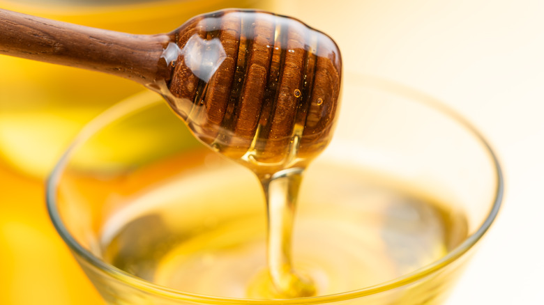 Wooden honey spool covered in honey, with more honey dripping back down into a glass bowl