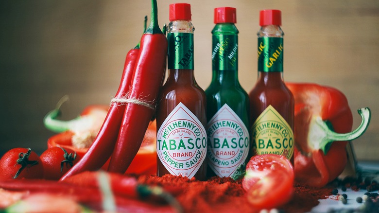 Three bottles of Tabasco surrounded by red peppers