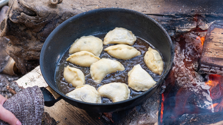 Person frying dumplings in melted butter over a campfire