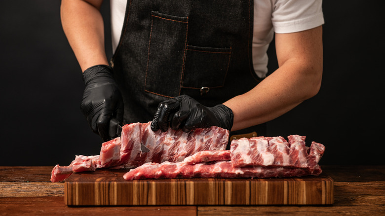 A person slicing through raw ribs.