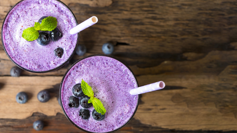 Blueberry smoothies sit on a wooden counter.