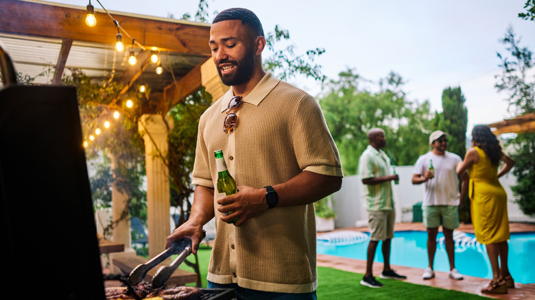 A person is seen handling tongs at a backyard grill.