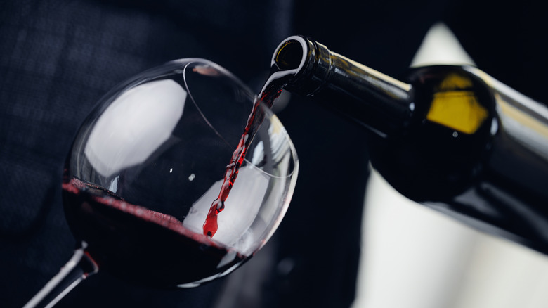 A bottle of red wine being poured into a crystal glass.