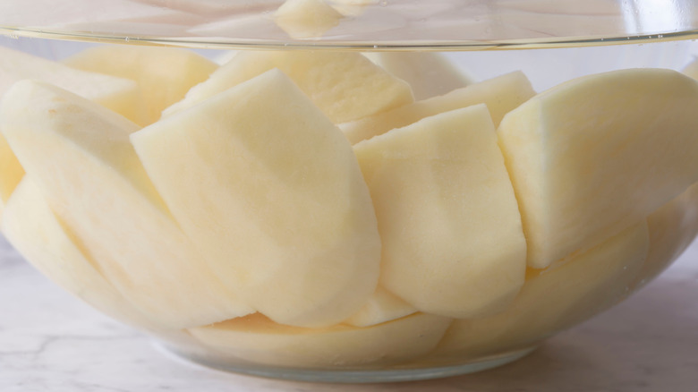 Sliced potatoes soaking in water in a glass bowl.