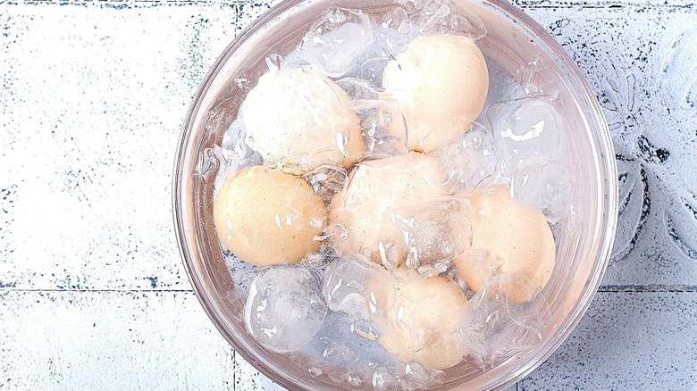 Six light brown eggs in a clear bowl of ice water over a white stone background