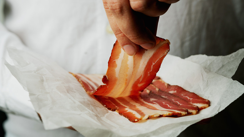 Fingers picking up a strip of bacon from paper
