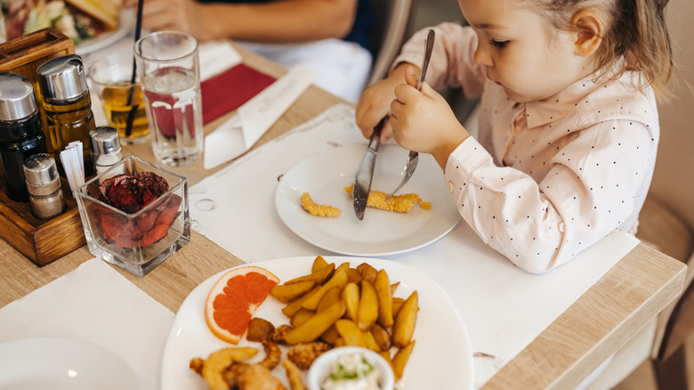 Child eating small amounts of fish and chips at a restaurant