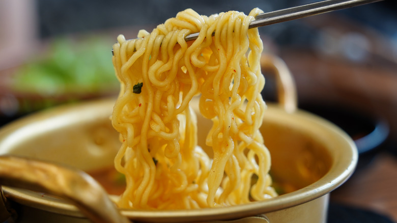 Noodles held in metal chopsticks over a bowl.