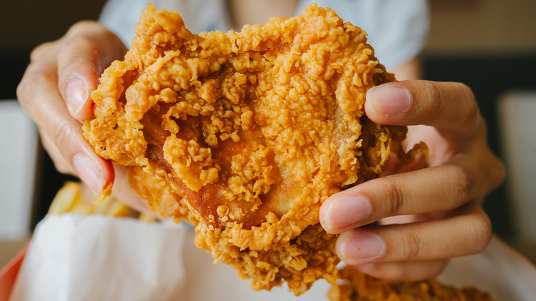 An individual holding a piece of crispy fried chicken.
