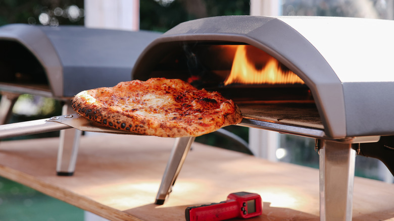 Cheese pizza being pulled out of outdoor pizza oven