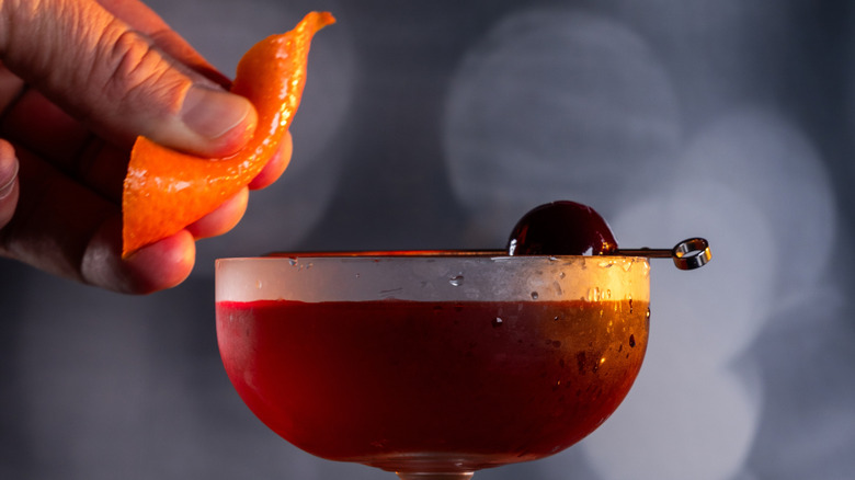 a Manhattan being garnished with cherry and orange