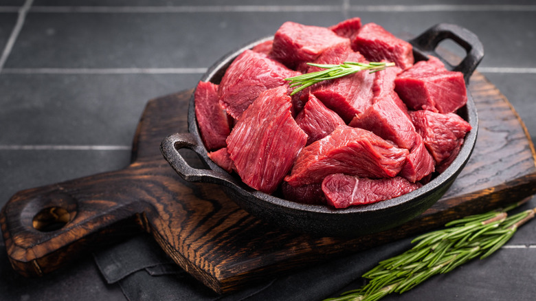 raw cubed beef in a cast iron pan with rosemary