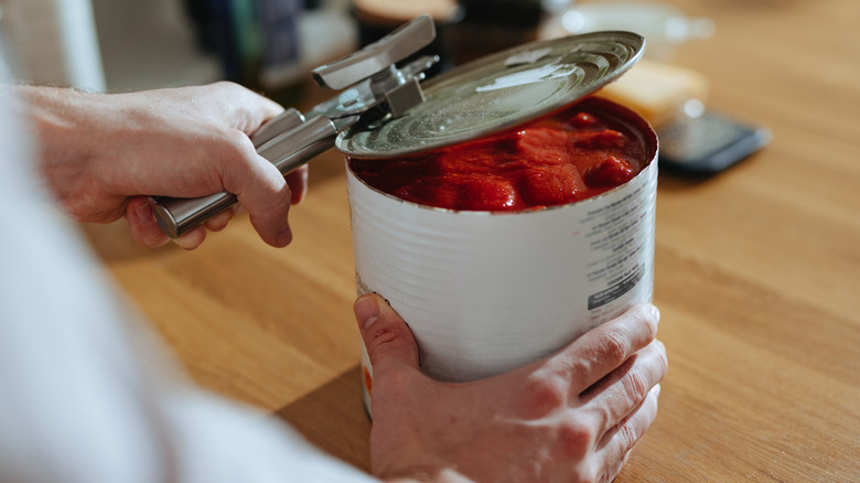 Person opening canned tomatoes
