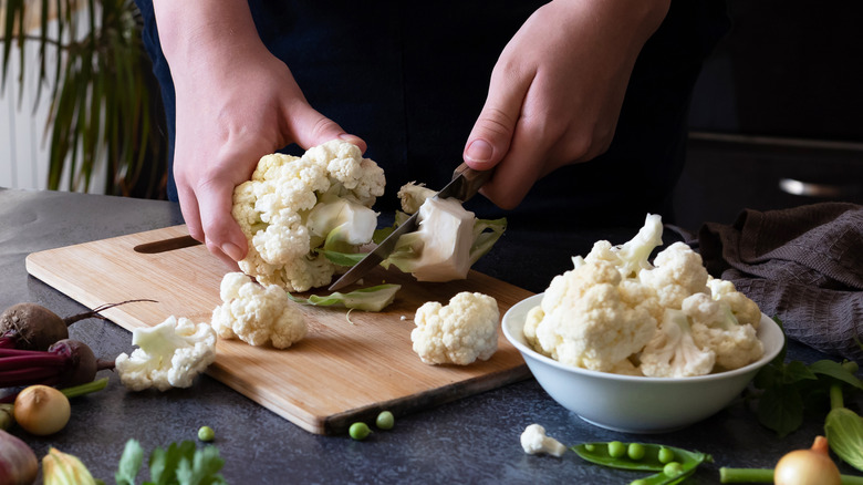 person cutting cauliflower on a cutting board