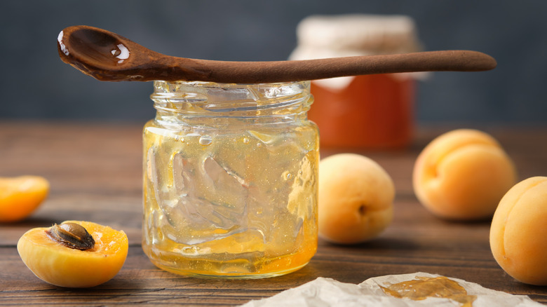 Empty jar of apricot jam with wooden spoon and fresh apricots around