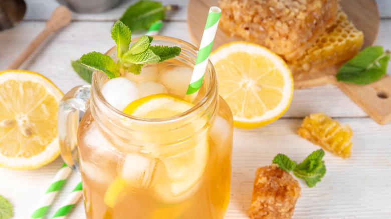 Citrus and honey cocktail in a mason jar with mint and striped green and white straw with honey, lemons, and mint surrounding.