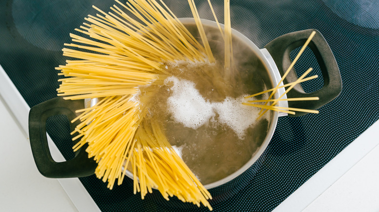 A top-down view of uncooked spaghetti noodles in a pot of steaming water